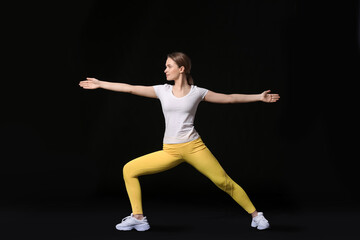 Sporty young woman doing yoga on dark background