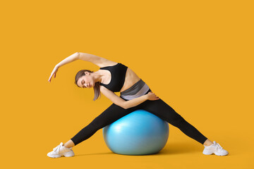 Sporty young woman training with fitball on color background