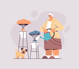 elderly woman watering flowers from watering can senior housewife taking care of house plants horizontal