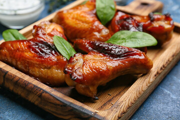 Board with roasted chicken wings on color background