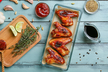 Baking dish with roasted chicken wings and sauces on color wooden background
