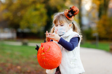 Little toddler girl dressed as a witch with medical mask on face trick or treating on Halloween....