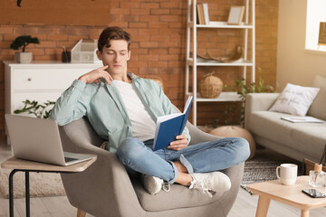 Young man reading book while sitting in armchair at home