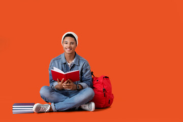 Male African-American student with book on color background