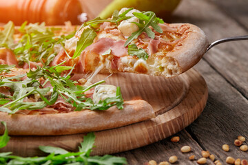 Slice of pizza with cured ham, blue cheese, pear, pine nuts, arugula