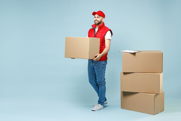 Full size body length delivery guy employee man in red cap white T-shirt vest uniform work as dealer courier hold blank cardboard box isolated on pastel blue color background studio. Service concept. - Powered by Adobe