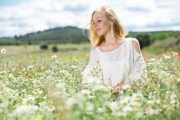Naklejka na ściany i meble Young woman wearing white dress posing in fields with daisies flowers outdoor