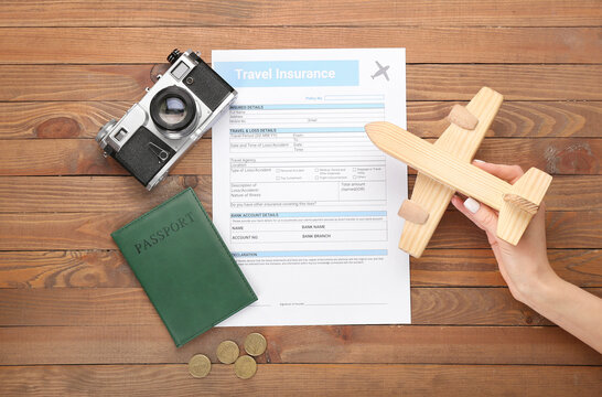 Female hand with wooden plane and travel insurance on wooden background