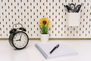 a black alarm clock, notepad and pen are placed on a white background of the table. five minutes past nine
