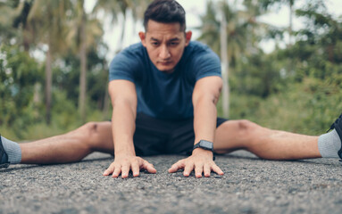 young man stretching in the park before running. Young man workout before fitness training at the park. Healthy and exercise young man warming up on the road in the forest.