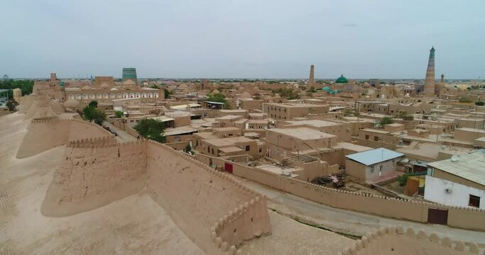 Aerial Forward Shot Of Religious Structures And Houses In Itchan Kala Surrounding Wall Against Clear Sky - Khiva, Uzbekistan