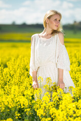 Naklejka na ściany i meble Young woman in yellow oilseed rape field posing in white dress outdoor