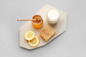 Fototapeta na wymiar Glass jar with sweet honey, lemon slices, comb and milk on grey background
