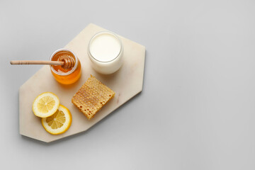 Glass jar with sweet honey, lemon slices, comb and milk on grey background