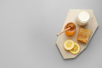 Fototapeta na wymiar Glass jar with sweet honey, lemon slices, comb and milk on grey background