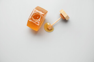 Jar with sweet honey and dipper on light background