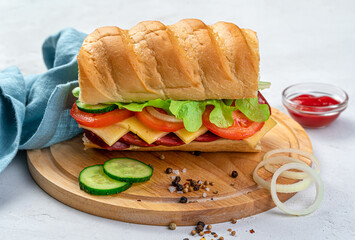 A large, delicious sandwich with fresh herbs, vegetables and sausage on a gray background.