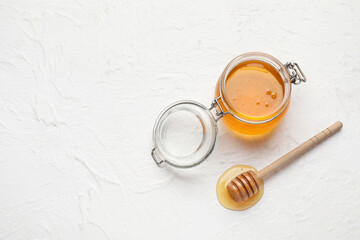 Glass jar with sweet honey and dipper on light background