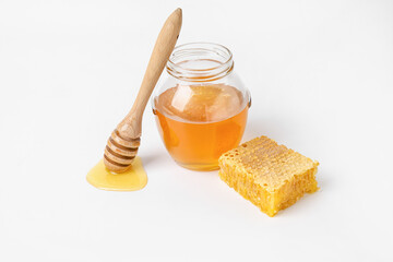 Glass jar with sweet honey, dipper and comb on white background