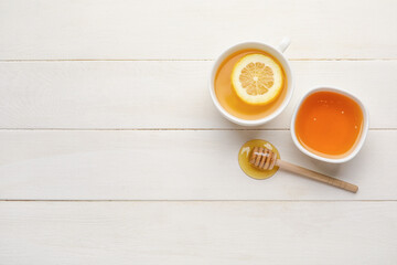 Bowl with sweet honey, dipper and cup of tea on light wooden background