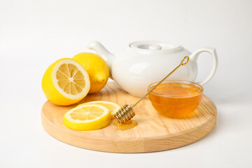 Glass bowl with sweet honey, lemon slices and teapot on wooden board against white background