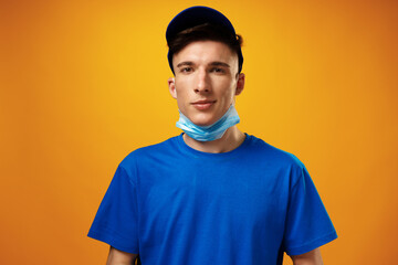 Young delivery man in green t-shirt and cap wearing face mask against yellow background