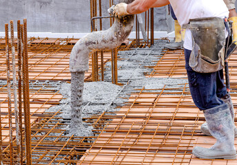 Building construction worker pouring cement or concrete with pump tube. Details of worker and...