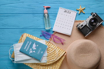 Calendar with beach accessories, medical masks and immune passport on color wooden background