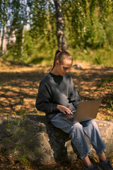 Fototapeta premium a young girl in nature in the forest sits on a rock and communicates online on the Internet via a laptop