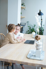 two girls sisters are sitting at home in front of the window at a laptop and arguing online training quarantine