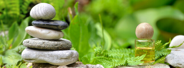 essential oil bottle next to a pile of  pebbles among green foliage in garden - obrazy, fototapety, plakaty