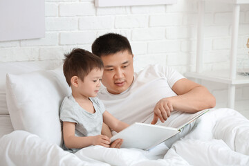 Fototapeta premium Father and his little son reading book in bedroom