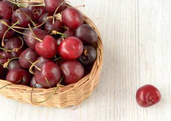 Red cherries lie in a wicker basket that stands on a wooden surface in light colors