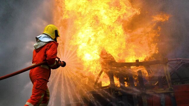 Professional Fireman in fire protection suit fighting strong fire in danger situation. Firefighter teamwork spray water from fire hose to extinguishing fire flames in training operation. 