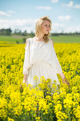 Fototapeta premium Young woman in yellow oilseed rape field posing in white dress outdoor