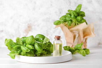Composition with fresh basil and bottle of essential oil on light background