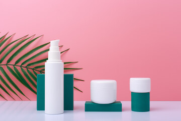 Trendy still life with set of beauty products for daily skin care with green geometric props on white table against pink background with palm leaf. Concept of natural organic cosmetic products 