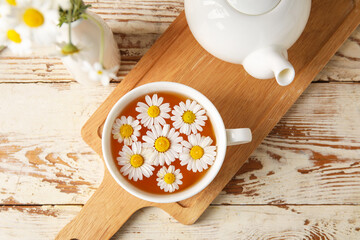 Composition with cup of chamomile tea and flowers on light wooden background