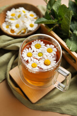 Composition with cup of chamomile tea, flowers and mint on color background