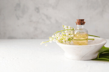 Bottle with essential oil and lily-of-the-valley flowers on light background