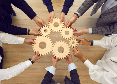 Professional business team connecting cogwheels as metaphor for good teamwork, synergy, effective cooperation and management. High angle, from above, top view closeup shot of human hands holding cogs