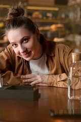 portrait of young smiling woman sitting in cafe staring to camera with question in her eyes