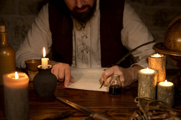 Medieval table with candles and a scroll, man writes with quill and ink