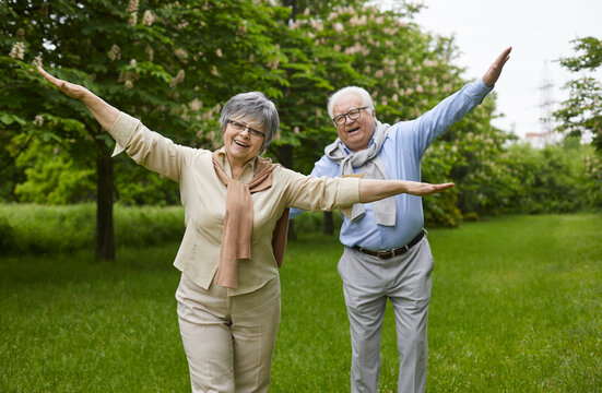 Happy senior couple enjoying life in retirement. Outdoor portrait of cheerful retired mature man and woman playing and having fun in a green summer park or city garden. Lifestyle concept