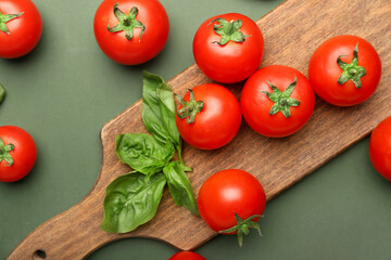 Board with fresh ripe tomatoes and basil leaves on color background