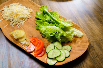 grated cheese, lettuce, ringed tomato and cucumber on a wooden cutting board.