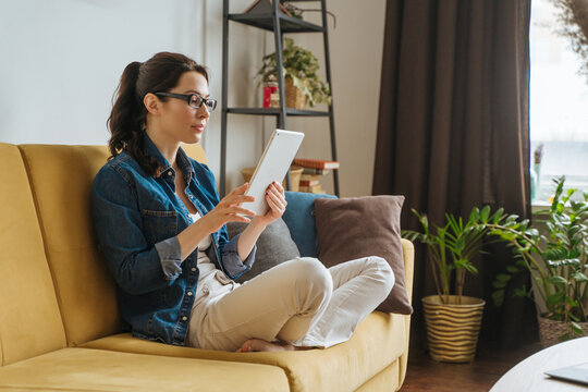 Happy woman reading a book in an ebook reader sitting on a couch at home