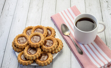 White cup with tea, teaspoon on a kitchen napkin, homemade cookies on a light wooden background. Concept of home breakfast, afternoon tea. Tea ceremony. Side and top view.