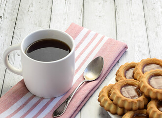 White cup with tea, teaspoon on a kitchen napkin, homemade cookies on a light wooden background. Concept of home breakfast, afternoon tea. Tea ceremony. Side and top view.