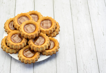 Homemade shortbread cookies with jam on a white plate on a light wooden background, close-up. Concept of breakfast, afternoon tea. Top and side view. Copy space.